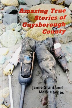 Book cover with text that reads: Amazing True Stories of Guysborough County. Authors Jamie Grant and Mark Haynes. The cover Image shows a rock beach with overalls, an artificial pirate's leg, a sword and rubber boot arranged to look like a torso.