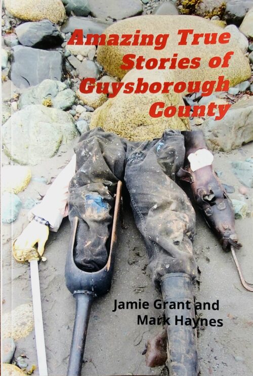 Book cover with text that reads: Amazing True Stories of Guysborough County. Authors Jamie Grant and Mark Haynes. The cover Image shows a rock beach with overalls, an artificial pirate's leg, a sword and rubber boot arranged to look like a torso.