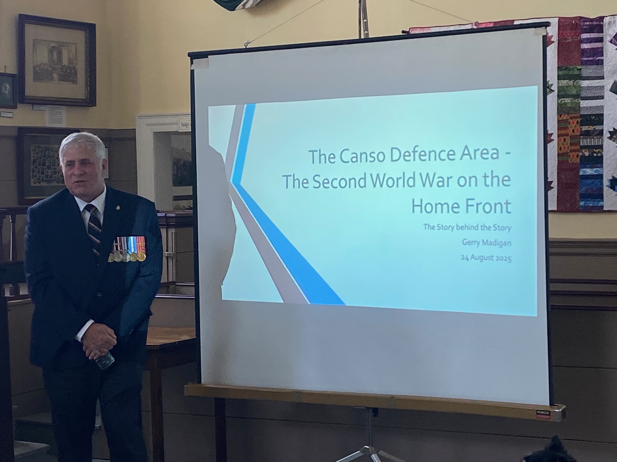 Gerry Madigan standing in front of Screen with PowerPoint presentation for Canso Defence zone book
