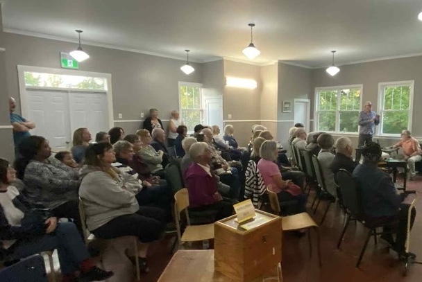 Audience seated listening to presenter (standing) in the Boylston Community Centre.