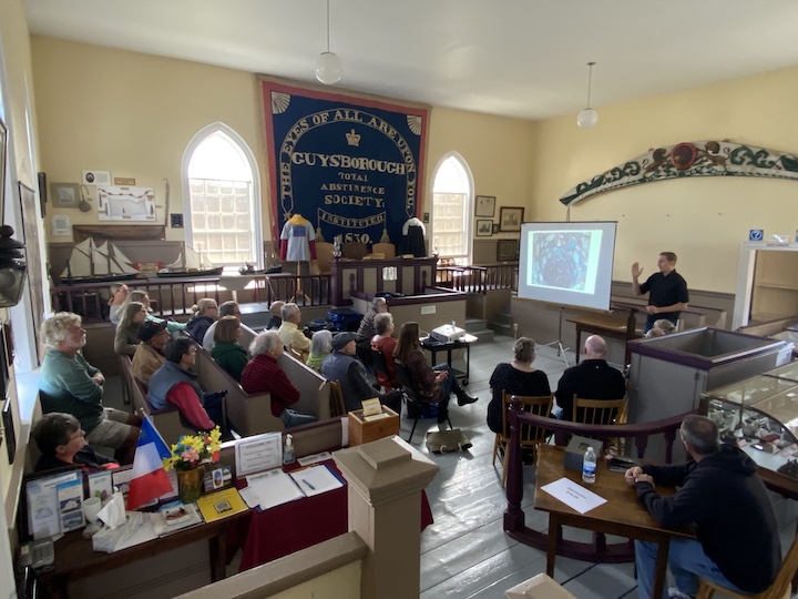 Audience in Old Courthouse Museum to the left in image, Steve Skafte to the right in image standing behind podium.