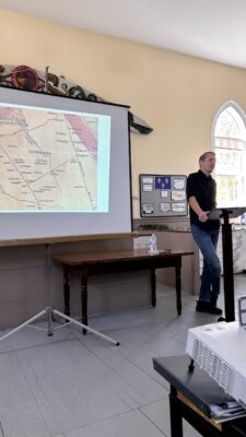 Presentation in Old Courthouse Museum showing a projected image on screen at left with Steve Skafte standing behind podium on the right.